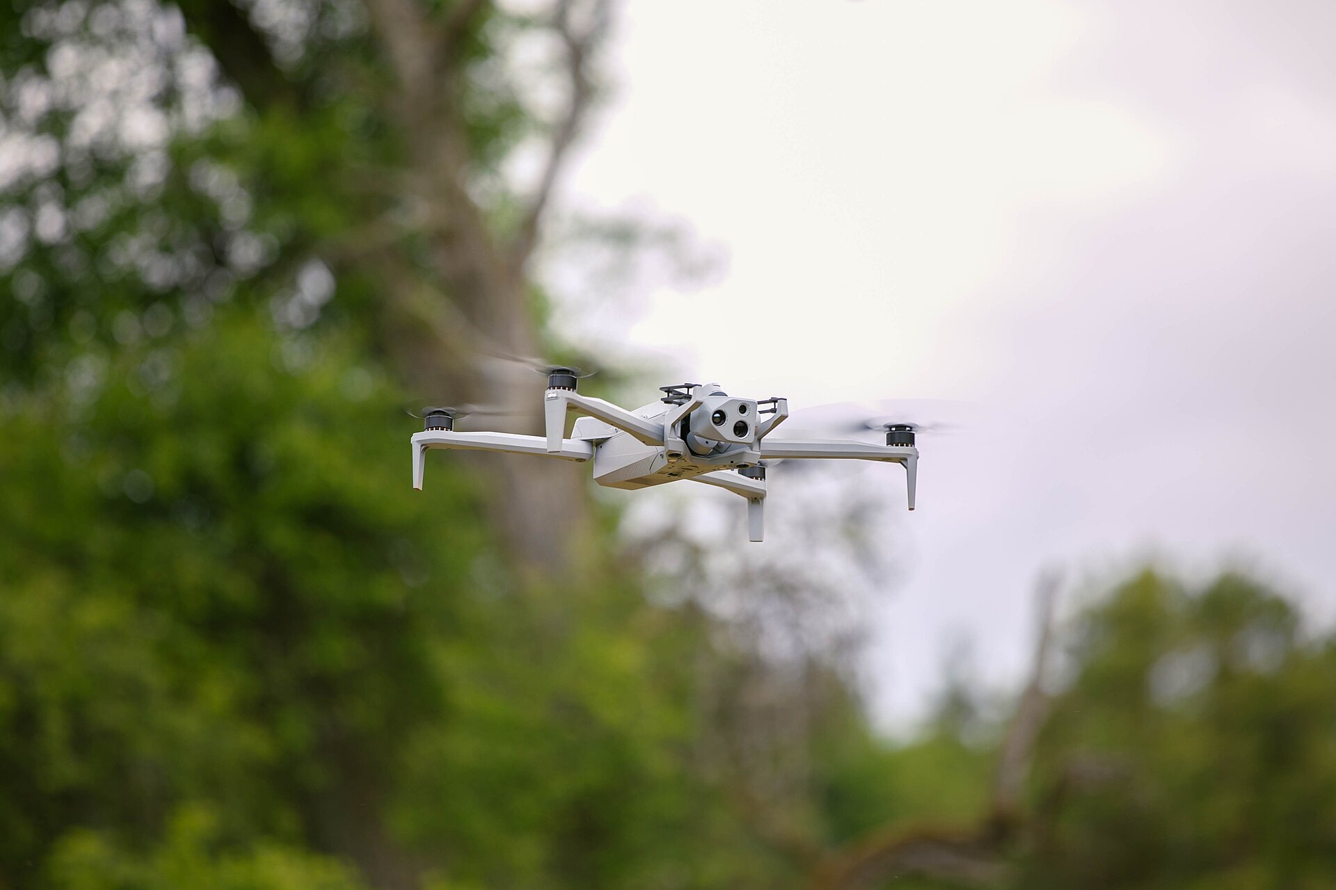 Skydio X10D banking in flight over wooded terrain during a field exercise